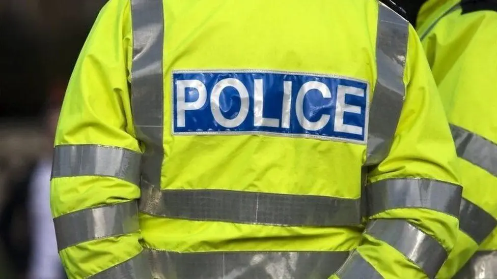 The back of a police officer wearing a high-vis police jacket.
